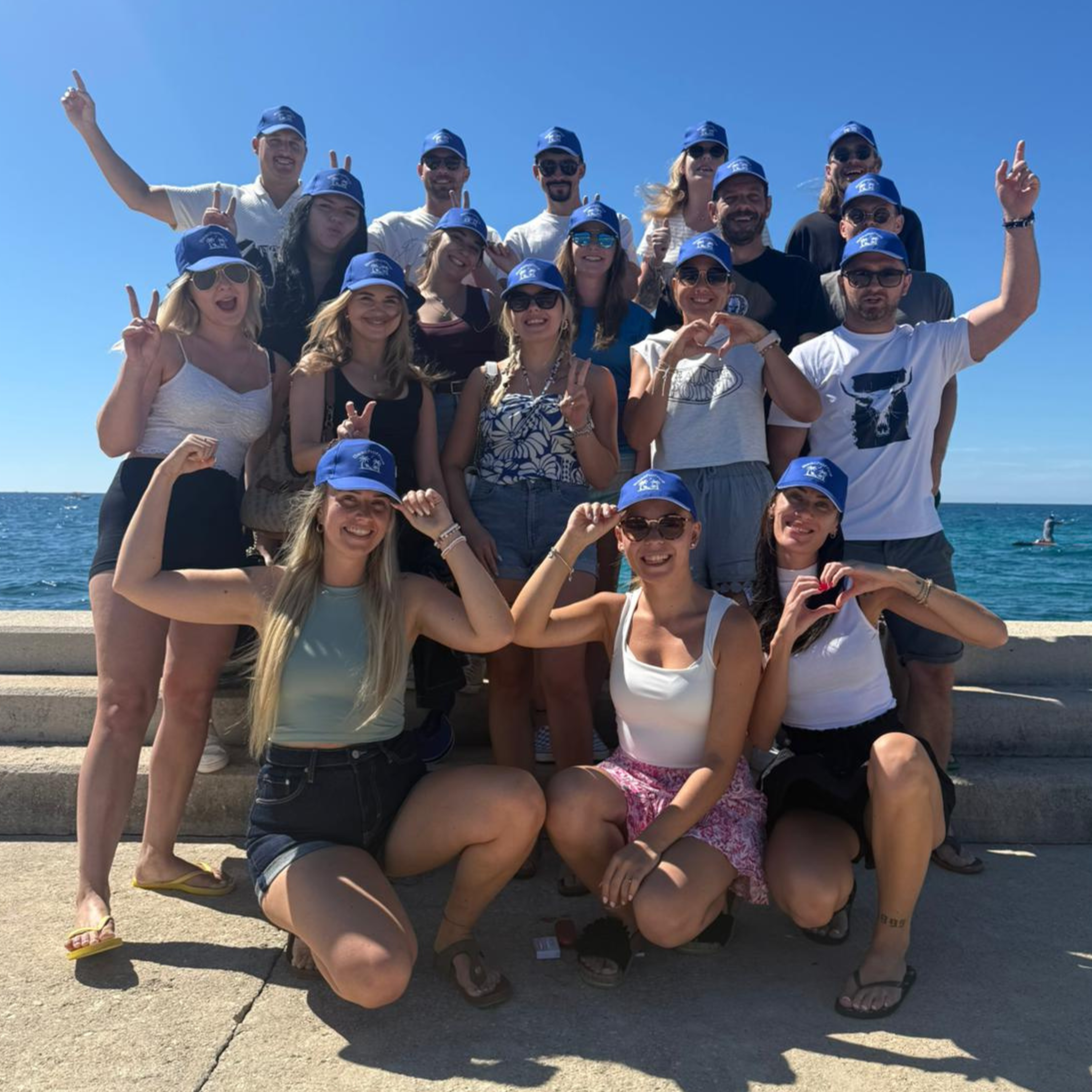 Das Team posiert gemeinsam am Meer mit einheitlichen blauen Kappen.